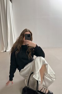 Zwarte sweatshirt, witte satijnen rok met ruches, zwarte handtas en zwarte sandalen met bandjes. Gladde texturen tegen contrasterende kleuren.