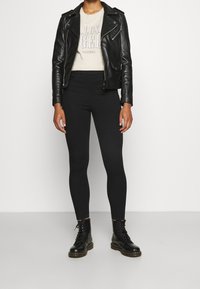Veste de motard en cuir noir portée sur un t-shirt clair avec le texte « Los Angeles », associée à des leggings noirs et des bottes de combat noires à lacets.