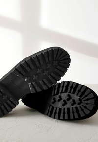 Musta kumipohja, jossa on syvät urat, reunat ja tähtimuotoiset koristeet parantamaan pitoa. Rakeinen pinta, kestävä materiaali.