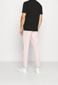 Svart polotröja och ljusrosa byxor, med smal passform. Slät tyg med en ren, minimal design. Vita sneakers kompletterar outfiten.