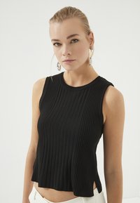 Zwarte mouwloze top met verticale ribbelstructuur, ronde halslijn en zijsplitten. Zachte stof, aansluitend boven de taille.