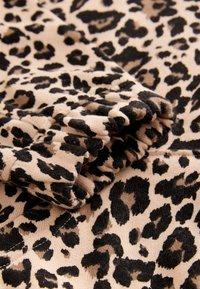 Material cu imprimeu de leopard, cu bază bej și pete negre, caracterizat printr-o textură moale și detaliu cu mansetă adunată.