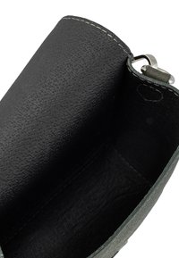 Interno di una borsa a tracolla in pelle nera, superficie texturizzata, cuciture grigie e un dettaglio in metallo argentato. Design aperto con una fodera liscia.