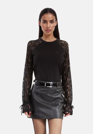 Zwart lang mouwen top met kantmouwen, gecombineerd met een zwarte leren minirok. De outfit heeft een zwarte riem met een zilveren gesp.