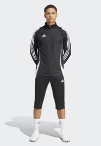 Svart treningszip-inngang med hvite side-striper, sorte shorts, og hvite sokker. Har Adidas-logo og glatt, fukttransporterende stoff.