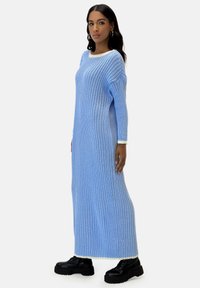 Rippenstrick-Maxikleid in Hellblau mit cremefarbenem Ausschnitt und Bündchen, kombiniert mit schwarzen, klobigen Schnürstiefeln für einen Kontrast.