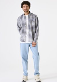 Heren overhemden met ruitpatroon in blauw en beige, met een button-down ontwerp. Gepaard met lichtblauwe jeans en beige sneakers, met een eenvoudig wit T-shirt.