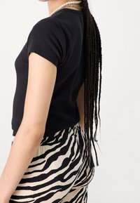 Black ribbed short-sleeve top paired with beige and black zebra-patterned pants. Notable details include a fitted design and smooth texture.