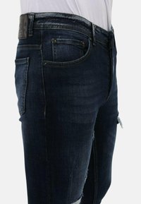Donkerdenim jeans met een slim fit, voorzien van distressed knie-details, vijf-pocket ontwerp en metalen hardware accenten bij de taille.
