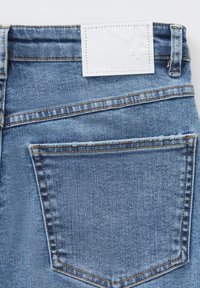 Jeans in denim blu chiaro con superficie testurizzata, dotati di un'etichetta bianca in vita e una sola tasca posteriore con cuciture visibili.