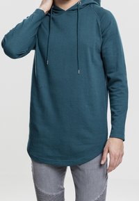 Felpa con cappuccio verde-blu con coulisse, maniche lunghe, orlo arrotondato e tessuto morbido, abbinata a pantaloni grigi con motivo.