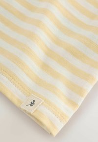 Yellow and white striped fabric with a smooth texture, featuring a small label with a plant design on the edge.