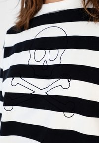 Chemise à rayures noir et blanc avec un fin contour de tête de mort et croix osseuses portée par une personne ayant les cheveux bruns.