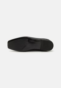 Suela de zapato negra plana con superficie suave, punta redondeada, ligera textura en la parte inferior para el agarre y detalle de marca en el costado.