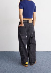 Klippt blå ribbad t-shirt med gula detaljer; svarta cargobyxor med flera fickor; bärs med gula och bruna sneakers.