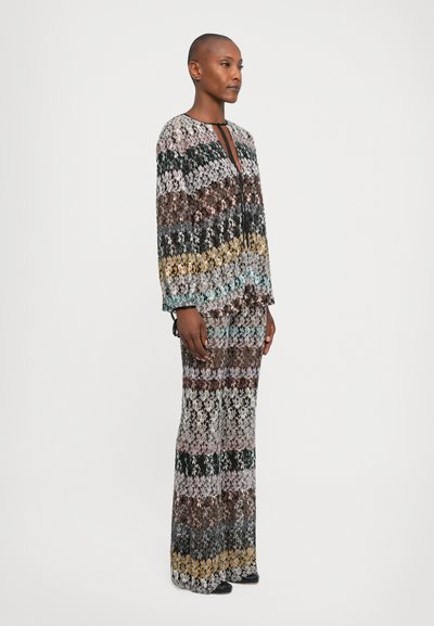 Standing woman wearing a long-sleeve, full-length knit outfit with multicolored horizontal floral patterns against a white background.