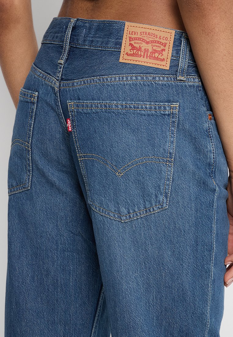 Jean en denim de couleur bleu foncé, avec cinq poches, un design à jambe droite et une étiquette en cuir de marque sur la taille arrière.