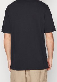 Černé tričko s krátkými rukávy a kulatým výstřihem, vyrobené z bavlny, s hladkou texturou a jednoduchým designem, zobrazuje zadní pohled.