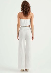 Vit två-delad outfit som består av en strapless topp med en samlad design och vida byxor med en texturerad yta.