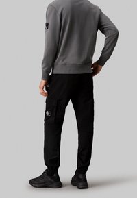 Grå sweatshirt med ribbade ärmar, kombinerad med svarta cargobyxor med sidficka och logotyp, bärs med svarta atletiska skor.