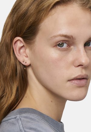 Ohrringe aus Roségold mit zwei kleinen Kugel-Studs und einem geschwungenen Hoop, die eine glatte, metallische Textur betonen.