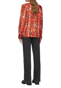 Rode blouse met slangenprint, lange mouwen en een ontspannen pasvorm, gecombineerd met donkergrijze wijde jeans en zwarte chunky laarzen.