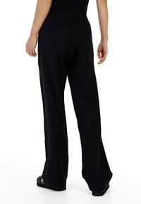 Zwarte wijde pantalons met een elastische tailleband, voorzien van twee achterzakken. De stof lijkt glad en duurzaam.