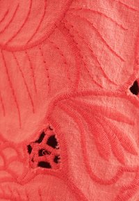 Koralikowy materiał z teksturowym haftem, przedstawiającym spiralne wzory liści; zawiera otwory dla szczegółów wizualnych i kontrastowe szycia.