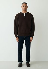 Brown ribbed knit sweater with a rounded hem, four-button placket. Worn with dark blue straight-leg jeans and brown loafers.