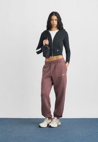 Musta lyhyt vetoketjuhuppari valkoisin yksityiskohdin, väljät burgundinpunaiset verkkarit ja beiget tennarit, joita täydentää pieni musta olkalaukku.