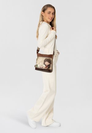 Braune Lederhandtasche mit einer verspielten Illustration und Text auf der Vorderseite, verstellbarem Riemen und Reißverschlussfächern.