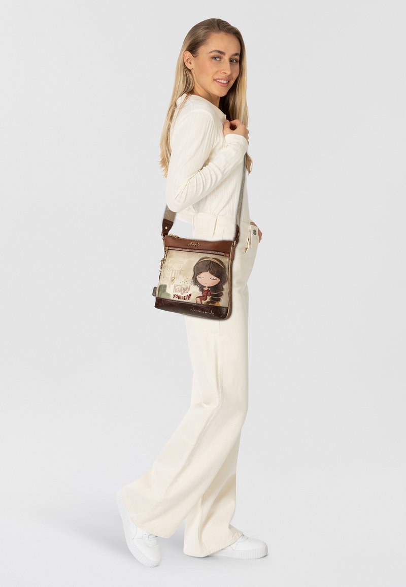 Braune Lederhandtasche mit einer verspielten Illustration und Text auf der Vorderseite, verstellbarem Riemen und Reißverschlussfächern.