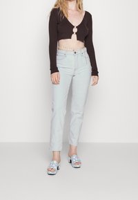 Top corto a coste marrone con un taglio circolare, jeans dritti azzurri e sandali blu con zeppa e motivo floreale.