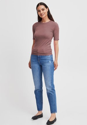 Brown short-sleeve top, fitted design. Blue jeans, straight leg, slightly distressed. Black flats. White background.