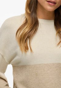 Beżowy sweter z blokami kolorystycznymi w odcieniach kremowego, wykonany z miękkiego dzianiny, z prążkowanym dekoltem i luźnym krojem, podkreślający fakturę i styl.