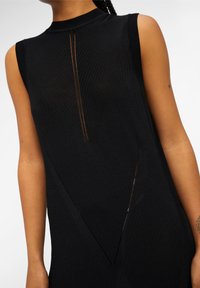 Robe noire en maille côtelée avec un col montant et un design sans manches. Présente des lignes verticales et des détails découpés qui mettent en valeur la texture.