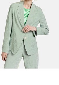 Blazer rayé vert avec un revers cranté, deux poches avant et une fermeture à un bouton. Porté sur un blouse en satin vert.