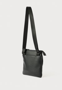 Čierna crossbody taška vyrobená z textúrovanej kože, s odnímateľným popruhom a zipsovým uzáverom. Obdĺžnikový tvar s minimalistickým dizajnom.