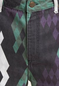 Multicolored jeans featuring a diamond pattern in green, black, and purple. Made of denim with a metal button closure.