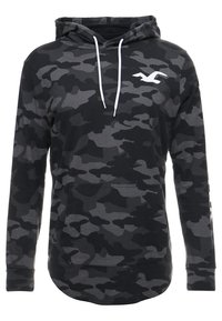 Huvtröja i svart och grå camouflage-mönster, med en framficka, vita dragsnören och en vit logotyp på bröstet.