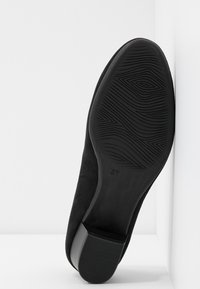 Chaussure en suede noire vue par dessous, dotée d'une semelle en caoutchouc texturé avec un grip à motifs et d'un petit talon carré. Taille indiquée comme 37.