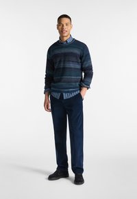 Maglione a righe blu scuro indossato sopra una camicia a righe blu chiaro, abbinato a pantaloni in corduroy blu navy e scarpe in suede nere.