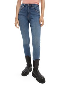 Jeans de denim azul ajustados con cintura alta, costuras contrastantes y un ligero desvanecimiento. Combinados con botas de tobillo negras.