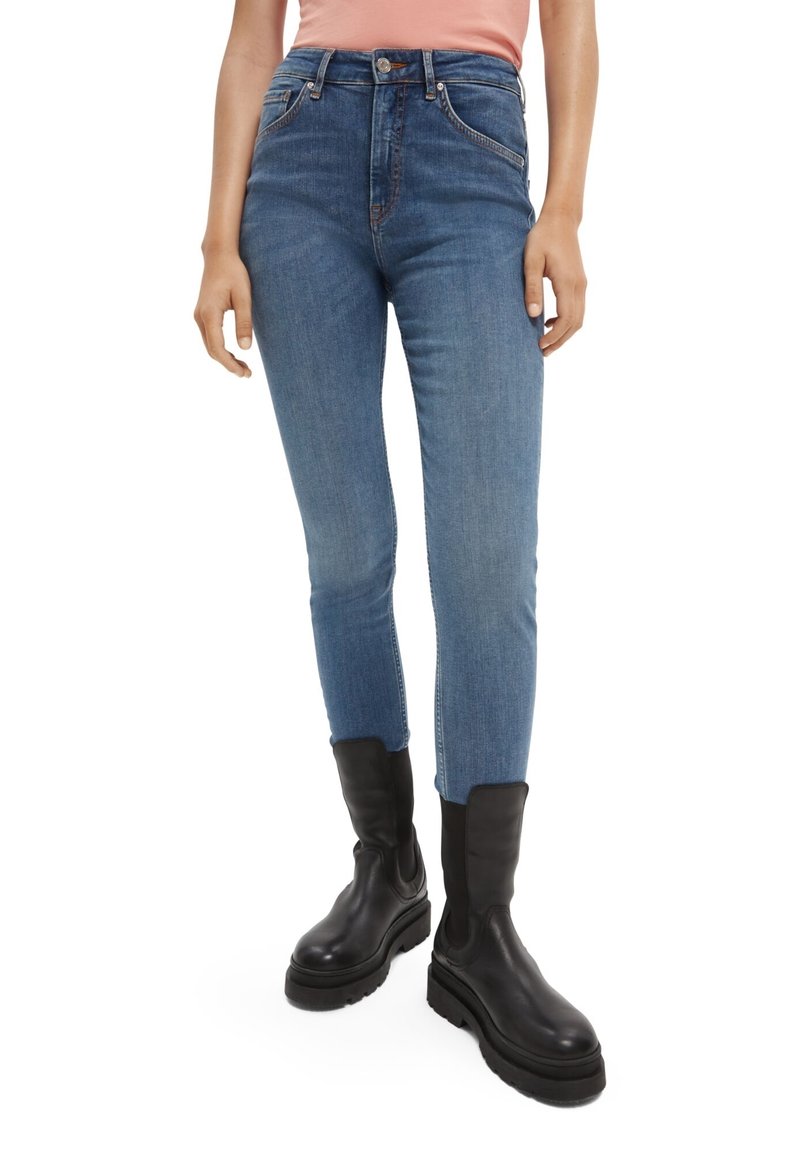 Jeans de denim azul ajustados con cintura alta, costuras contrastantes y un ligero desvanecimiento. Combinados con botas de tobillo negras.