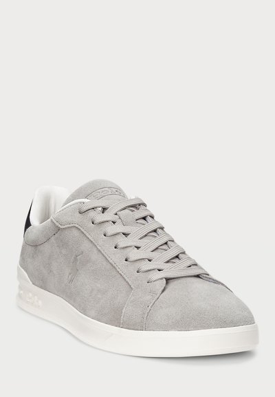 Lys grå semsket lavtopp sneakers med hvit såle, grå lisser, polstret krage, og subtilt preget logo på siden og tungen.