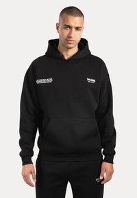 Czarna bluza z kapturem wykonana z miękkiego materiału, wyposażona w kieszeń kangurkę, ściągacze na rękawach oraz białe nadruki. Klasyczny, luźny krój.