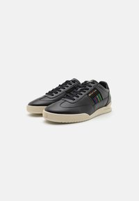 Zapatillas de cuero negras con un diseño cónico y suela beige en contraste. Presenta rayas verticales de colores y cordones negros.