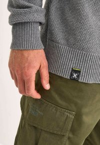 Maglione grigio testurizzato con polsini a costine, abbinato a pantaloni cargo verde oliva con tasca laterale e logo del marchio.