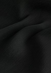 Tessuto nero con una superficie texturizzata e leggermente rugosa. Il materiale appare leggero e flessibile, mostrando sottili variazioni di lucentezza.