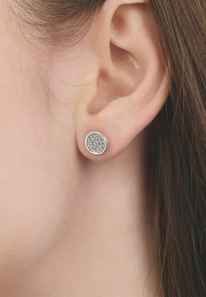 Zbliżenie na ucho noszące okrągły, srebrny kolczyk z małymi, przezroczystymi kryształkami.
